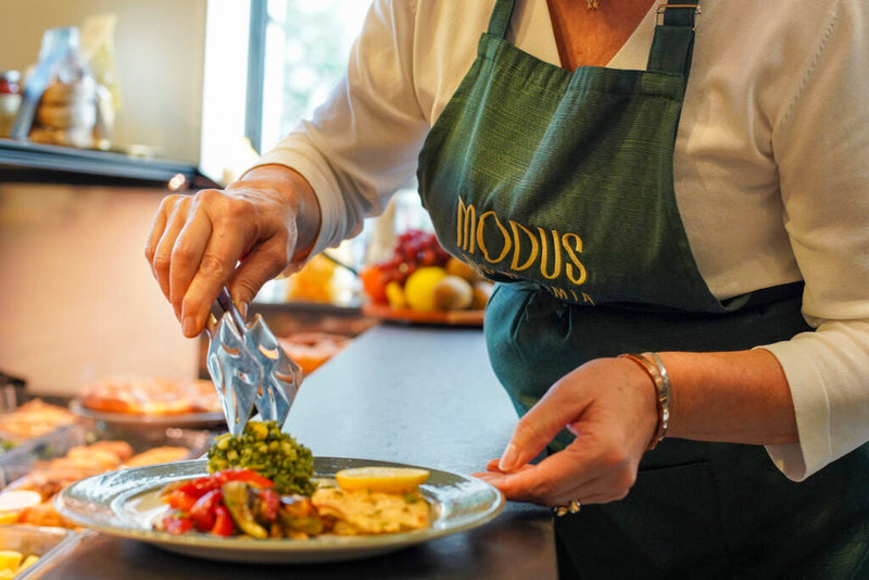 Addetta della gastronomia Modus che impiatta un piatto di carne e verdure con le pinze