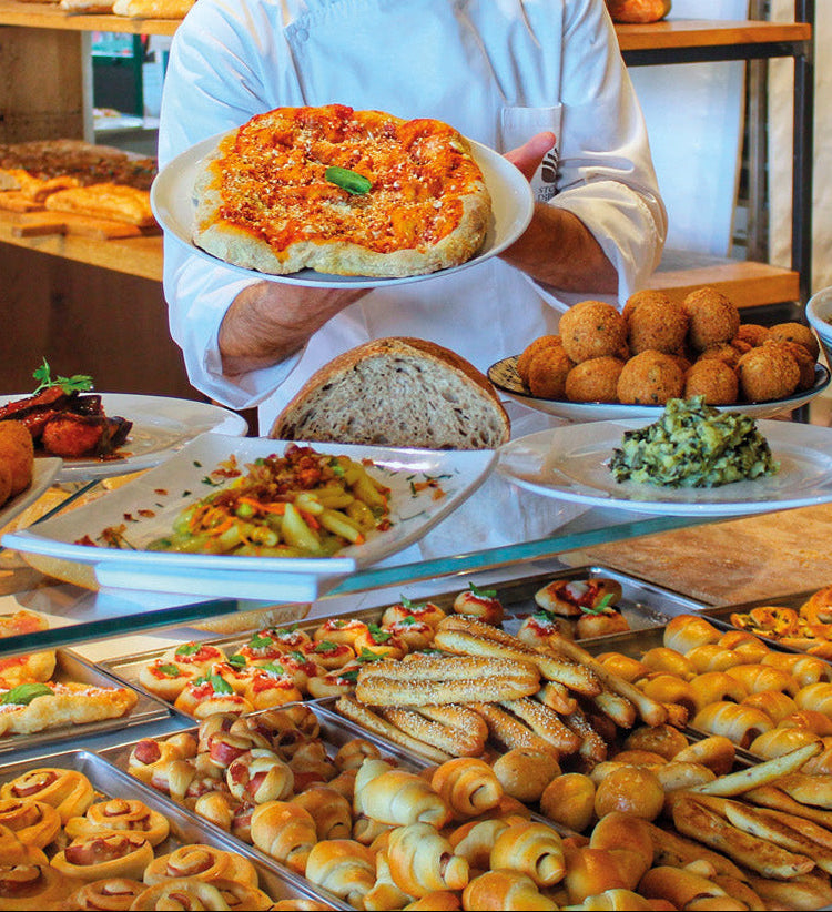 Banco della gastronomia Modus con crocchè, verdure e piatti pronti, e un addetto che serve un piatto