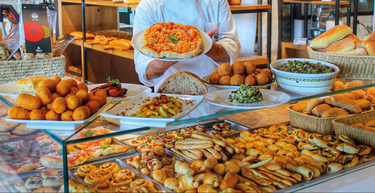 Banco della gastronomia Modus con crocchè, verdure e piatti pronti, e un addetto che serve un piatto