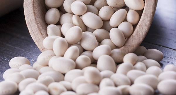 Fagioli bianchi che escono da una ciotola di legno