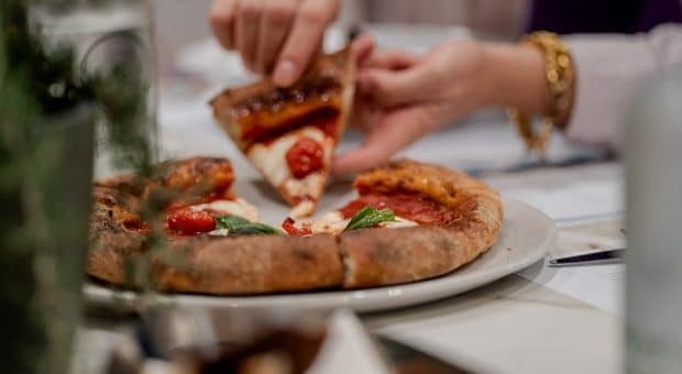Mani che tagliano una pizza al pomodoro