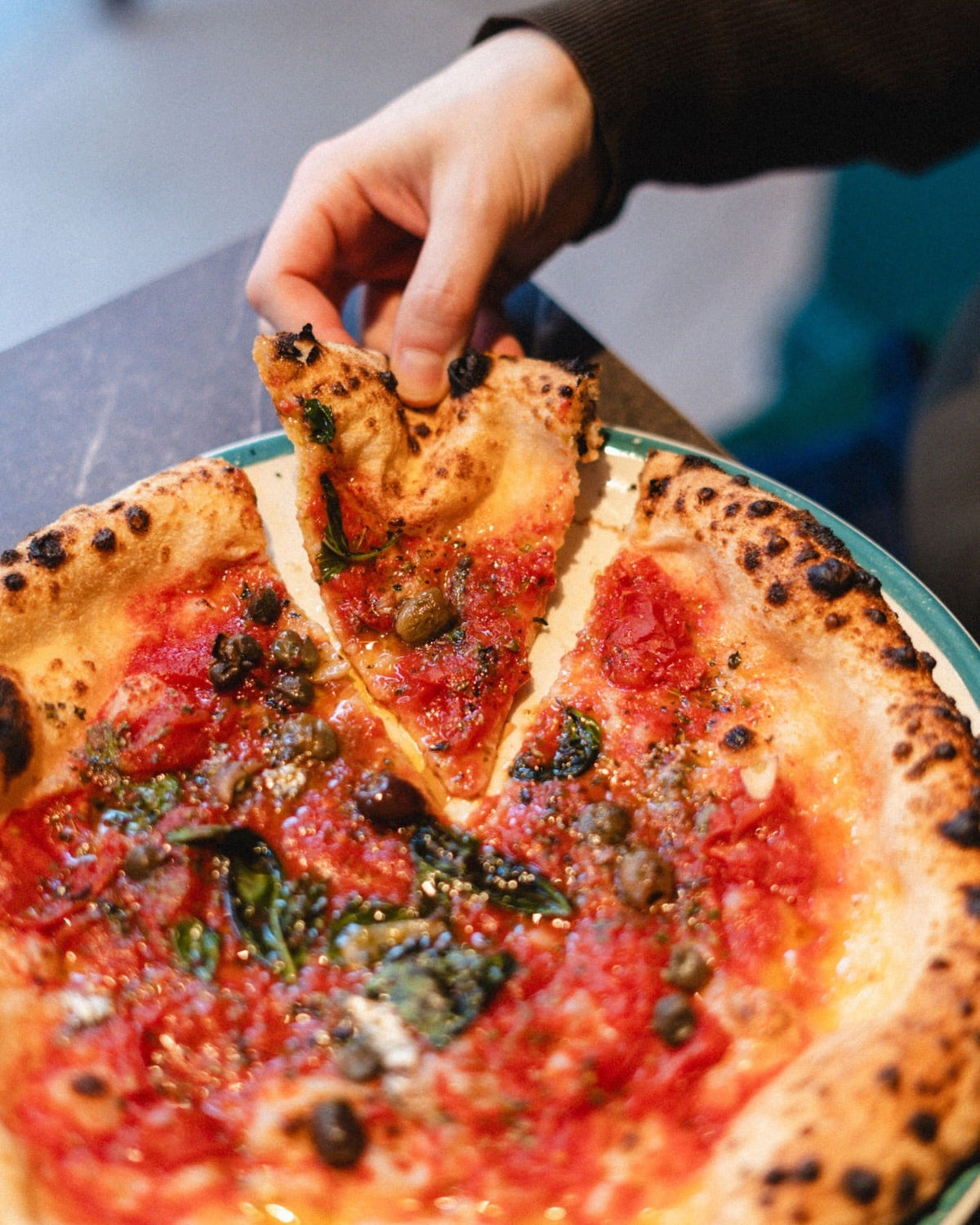 Mano che stacca una fetta da una pizza al pomodoro