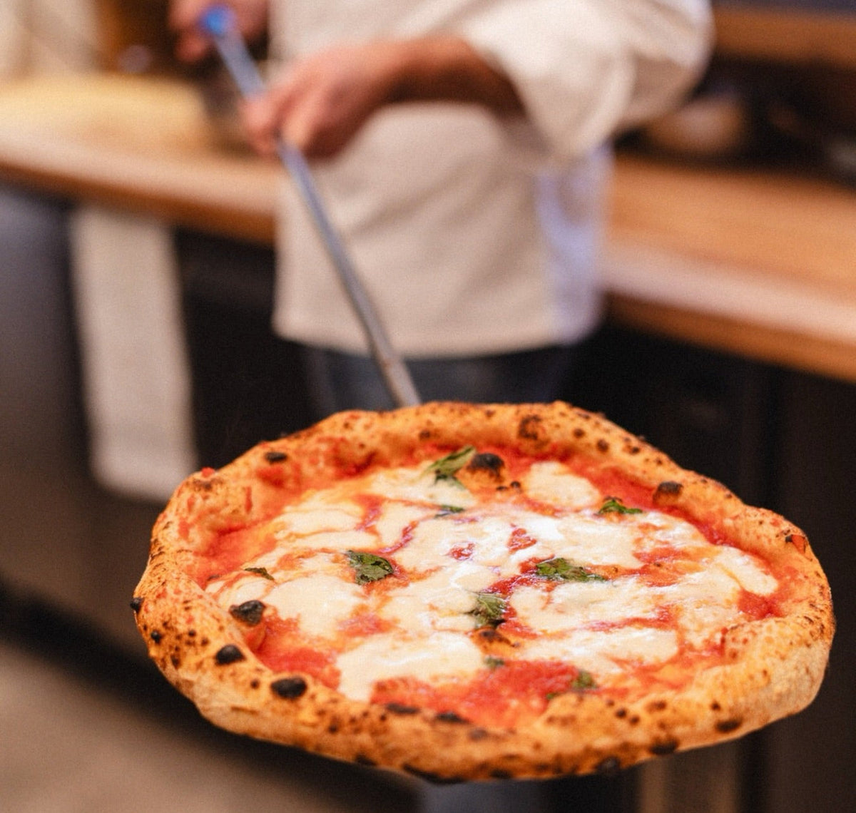 Pizza margherita sollevata con la pala da un pizzaiolo
