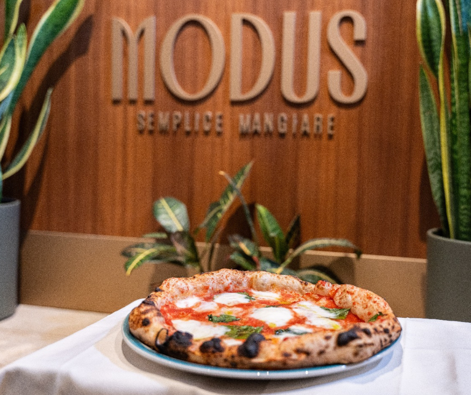 Pizza margherita su un piatto davanti all'insegna Modus Semplice Mangiare