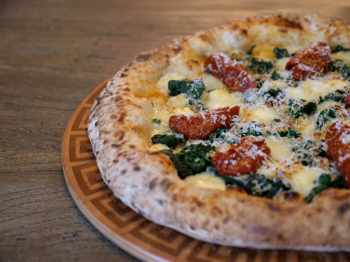 Pizza con verdure, pomodorini e mozzarella su un tagliere di legno