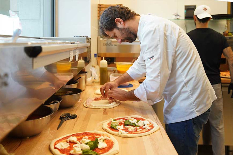 Pizzaiolo al lavoro in cucina, con pizze margherita sul banco