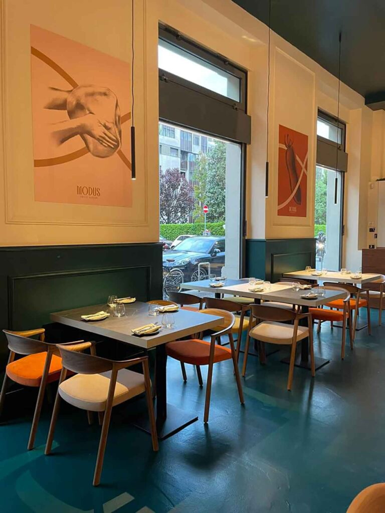 Sala della pizzeria Modus con tavoli, sedie arancioni e pareti verde petrolio
